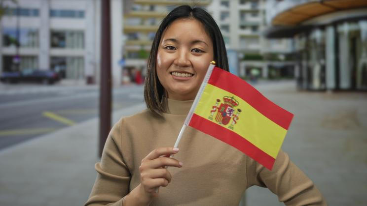 Woman,Smiling,While,Holding,A,Spanish,Flag,On,A,City