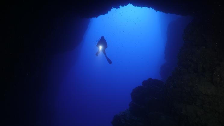 Scuba,Divers,Underwater,Exploring,Caves,Blue,Ocean,Scenery,With,Torch