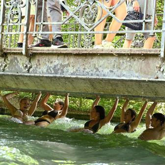 People swim along with the current of the Eisbach in the English Garden all the way to the nearest tram stop in Munich