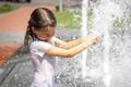 ["Funny little girl in the fountain plays with splashes of water."]