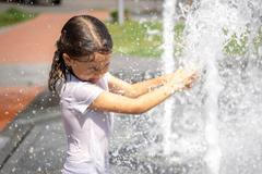 ["Funny little girl in the fountain plays with splashes of water."]