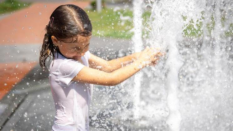 ["Funny little girl in the fountain plays with splashes of water."]