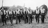 Skupina pilotů slavné polské 303. stíhací perutě kráčí od letounu Hawker Hurricane, ze kterého se podle všeho právě vrátili z bojového letu. Zleva doprava v první řadě: poručík Mirosław Ferić, kapitán John A. Kent (velitel letky „A“), nadporučík Bogdan Grzeszczak, poručík Jerzy Radomski, poručík Witold Łokuciewski, poručík Bogusław Mierzwa (zakrytý Łokuciewským), nadporučík Zdzisław Henneberg, rotmistr Jan Rogowski a rotmistr Eugeniusz Szaposznikow. Uprostřed v pozadí, v letecké kukle a brýlích, stojí poručík Jan Zumbach.