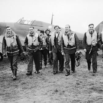 Skupina pilotů slavné polské 303. stíhací perutě kráčí od letounu Hawker Hurricane, ze kterého se podle všeho právě vrátili z bojového letu. Zleva doprava v první řadě: poručík Mirosław Ferić, kapitán John A. Kent (velitel letky „A“), nadporučík Bogdan Grzeszczak, poručík Jerzy Radomski, poručík Witold Łokuciewski, poručík Bogusław Mierzwa (zakrytý Łokuciewským), nadporučík Zdzisław Henneberg, rotmistr Jan Rogowski a rotmistr Eugeniusz Szaposznikow. Uprostřed v pozadí, v letecké kukle a brýlích, stojí poručík Jan Zumbach.