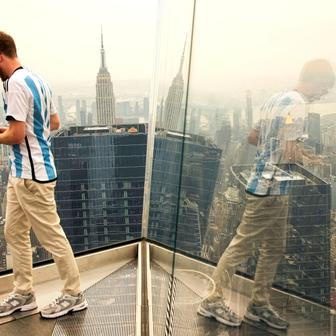 A person takes pictures as the New York City skyline and the Empire State Building are seen from the Edge observation deck through a cover of wildfire smoke in New York
