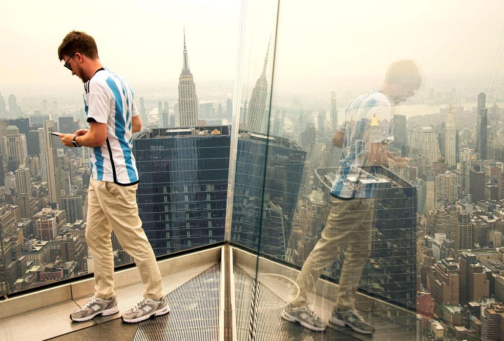 A person takes pictures as the New York City skyline and the Empire State Building are seen from the Edge observation deck through a cover of wildfire smoke in New York