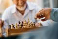Close,Up,Of,Seniors,Playing,Chess,On,Patio,In,Nursing