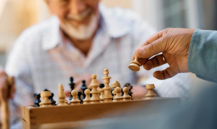 Close,Up,Of,Seniors,Playing,Chess,On,Patio,In,Nursing