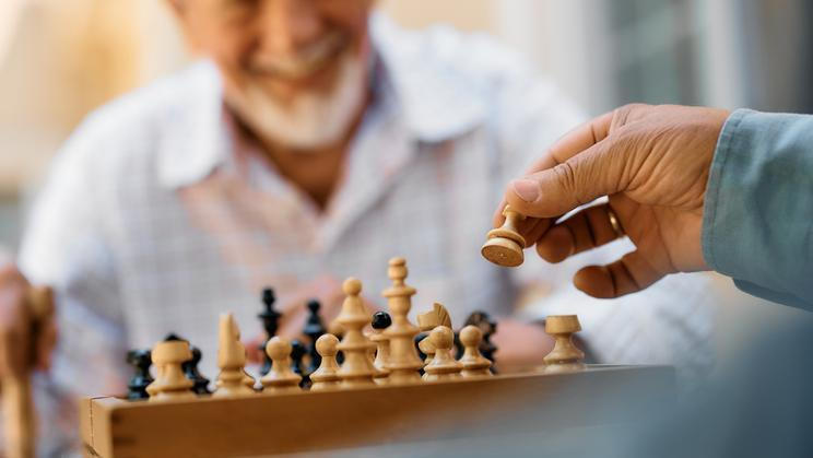 Close,Up,Of,Seniors,Playing,Chess,On,Patio,In,Nursing