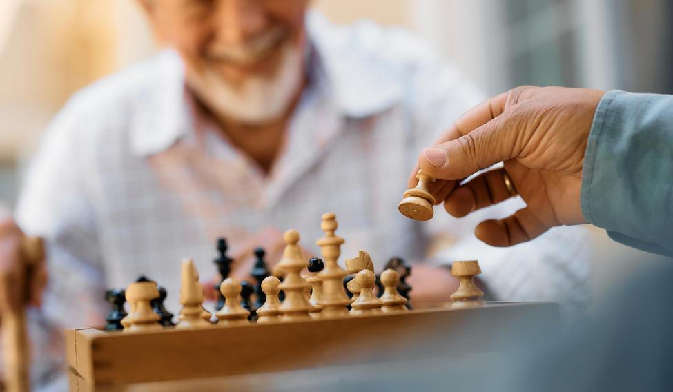 Close,Up,Of,Seniors,Playing,Chess,On,Patio,In,Nursing