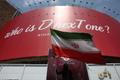 A woman holds an Iranian flag next to a billboard threatening U.S. President Donald Trump is displayed on a building in Tehran