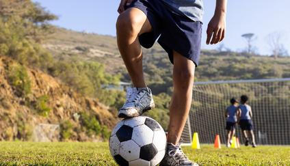 Outdoors, playing soccer on field, multiracial boys practicing with ball and cones
