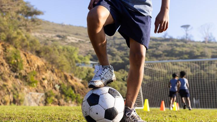 Outdoors, playing soccer on field, multiracial boys practicing with ball and cones