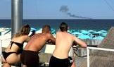 People look at a ship burning at sea in Odesa