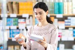Young,Woman,Standing,Near,Shelves,With,Medicines,And,Choosing,Boxes