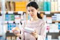 Young,Woman,Standing,Near,Shelves,With,Medicines,And,Choosing,Boxes