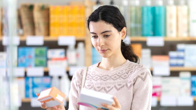 Young,Woman,Standing,Near,Shelves,With,Medicines,And,Choosing,Boxes