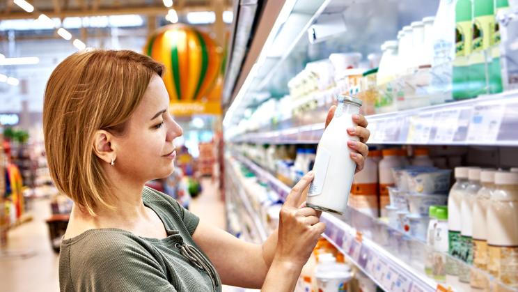 Young,Woman,Buyer,Chooses,Milk,In,Bottle,In,Grocery,Store