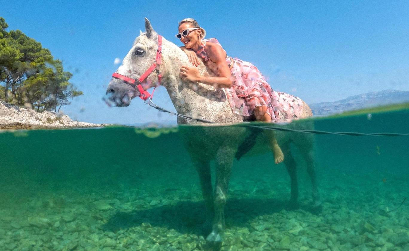 A woman poses on a horse named 'Perlaz' after swimming with it during the heatwave in Supetar on the island of Brac