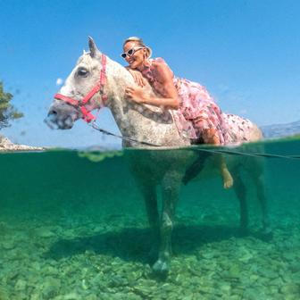 A woman poses on a horse named 'Perlaz' after swimming with it during the heatwave in Supetar on the island of Brac