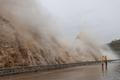 People stand next to huge waves crashing on a waterfront, as Typhoon Dolphin approaches, in Sanmen County, Zhejiang Province
