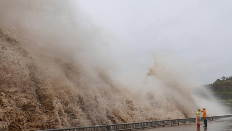 People stand next to huge waves crashing on a waterfront, as Typhoon Dolphin approaches, in Sanmen County, Zhejiang Province