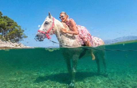 A woman poses on a horse named 'Perlaz' after swimming with it during the heatwave in Supetar on the island of Brac