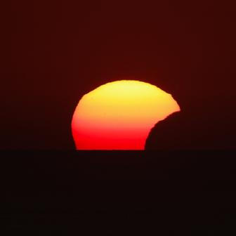 People watch a partial solar eclipse at sunset in Dingli