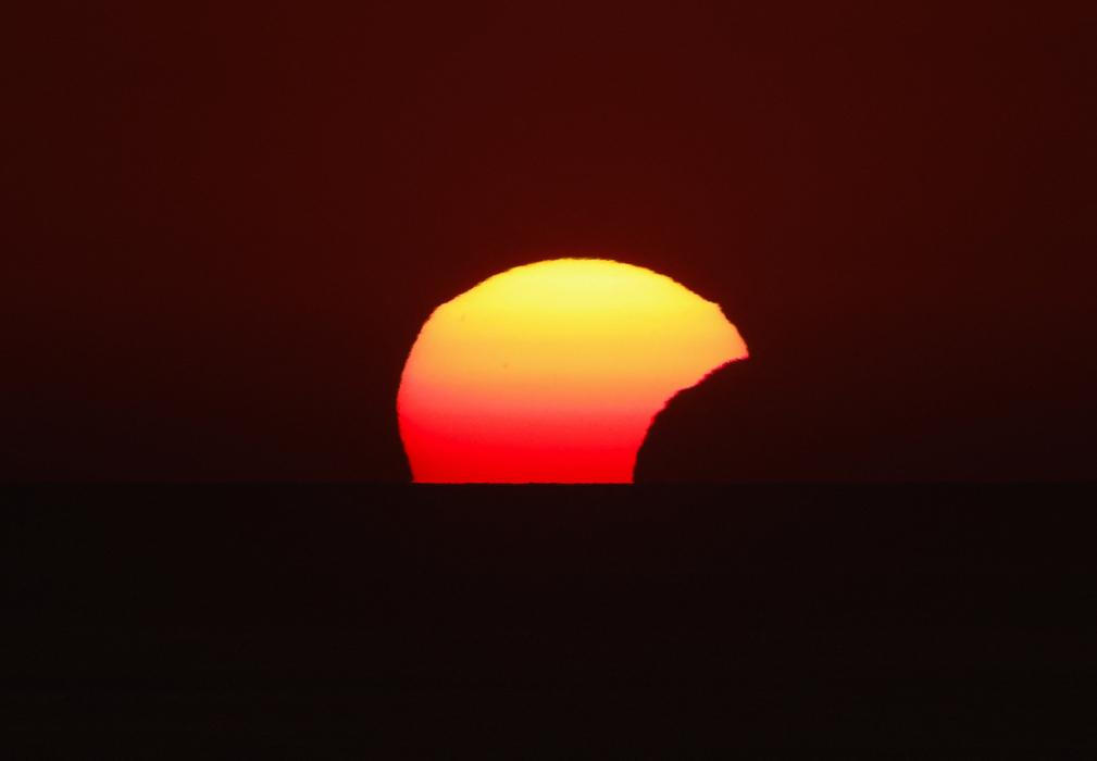 People watch a partial solar eclipse at sunset in Dingli