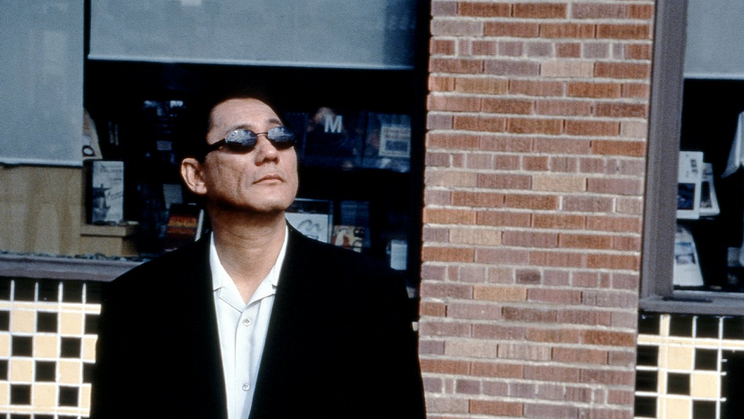 Takeši Kitano začínal jako stand-up komik v jenom z tokijských barů pod uměleckým jménem Beat Takeši. Dnes je známý jako filmový režisér, herec, komik, scénárista, moderátor, spisovatel a také malíř. Na snímku ve filmu Ve spárech yakuzy.