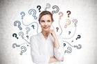 Cheerful,Young,Businesswoman,Standing,Near,Concrete,Wall,With,Question,Marks