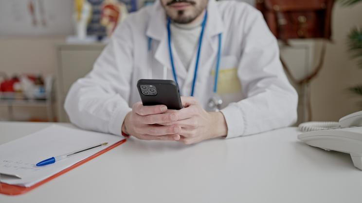 Young,Hispanic,Man,Doctor,Using,Smartphone,Working,At,Clinic