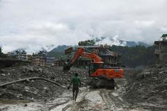 An excavator clears a muddy path after flash floods and a mudslide in Trishuli