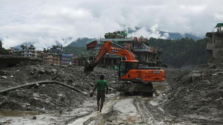 An excavator clears a muddy path after flash floods and a mudslide in Trishuli