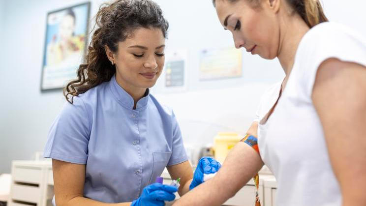 ["Medical technologist doing a blood draw services for patient. lab assistant with sterile rubber gloves taking blood sample from patient."]