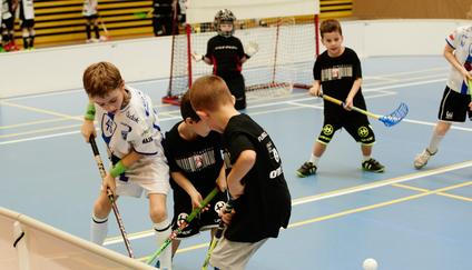 Children boys schoolchildren playing floorball (floor hockey) match in school gym hall with plastic hockey sticks