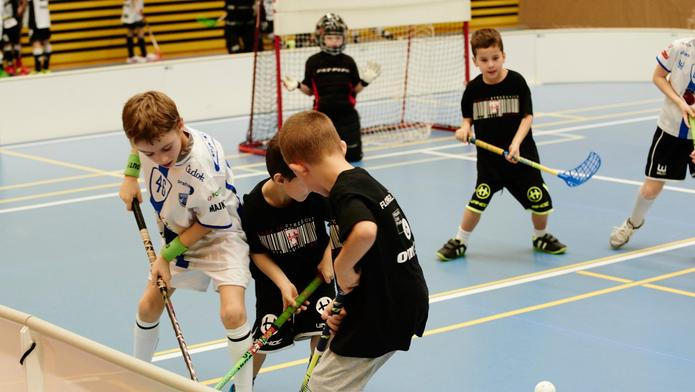 Children boys schoolchildren playing floorball (floor hockey) match in school gym hall with plastic hockey sticks