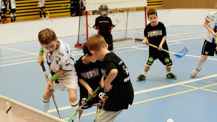 Children boys schoolchildren playing floorball (floor hockey) match in school gym hall with plastic hockey sticks