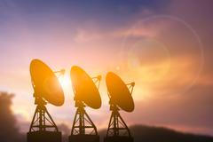 Three,Large,Satellite,Radar,Dishes,Standing,In,A,Row,,Silhouetted