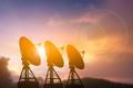 Three,Large,Satellite,Radar,Dishes,Standing,In,A,Row,,Silhouetted