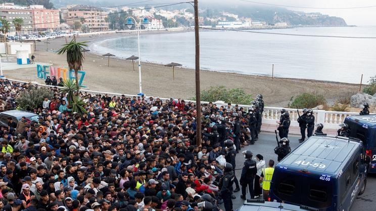 Police escort migrants from Benitez Beach to be relocated to the camp set up at the port of Ceuta