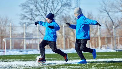 Developing ball control. Boys in blue jackets practicing dribbling on outdoor stadium with patches of snow. Precision and coordination training.