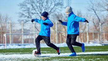Developing ball control. Boys in blue jackets practicing dribbling on outdoor stadium with patches of snow. Precision and coordination training.