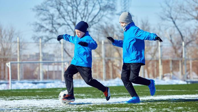Developing ball control. Boys in blue jackets practicing dribbling on outdoor stadium with patches of snow. Precision and coordination training.