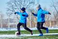 Developing ball control. Boys in blue jackets practicing dribbling on outdoor stadium with patches of snow. Precision and coordination training.